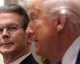 Two men in suits; focus on a serious-looking man wearing glasses, with a blurred man beside him wearing light hair.