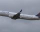 United Airlines passenger jet in flight with blue globe logo on tail, white fuselage, over a cloudy sky.