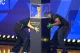 FIFA World Cup Trophy in a glass case on a black pedestal as two people crouch nearby on a blue-lit stage.