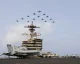 Fighter jets flying in formation over a US aircraft carrier