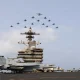 Fighter jets flying in formation over a US aircraft carrier